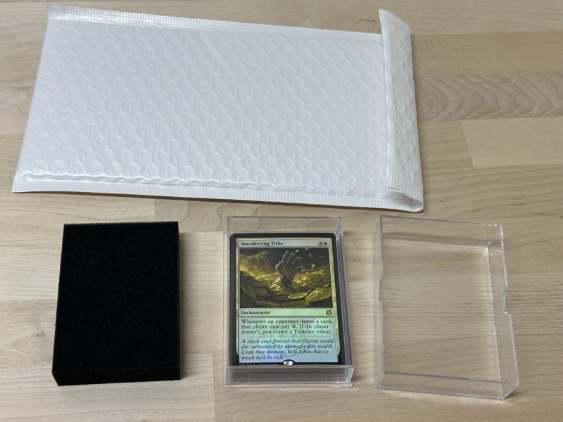 Shipping components laid out: a bubble mailer, a rigid deck box, and a card in a toploader