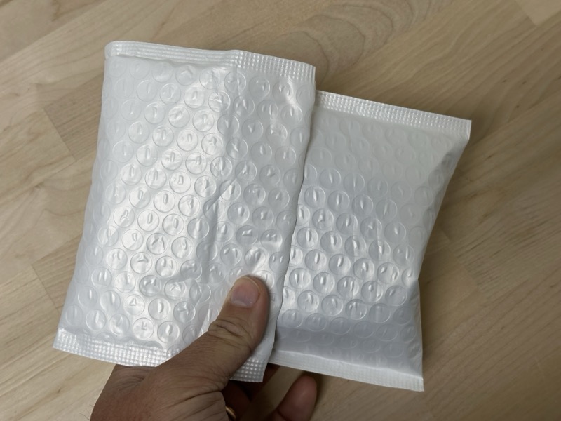 Sealed bubble mailer with deck box inside, held in hand showing compact size
