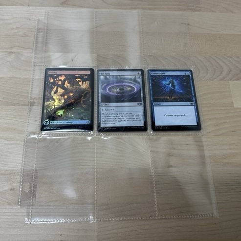 Three cards in toploaders placed inside a cut binder page sleeve for protection